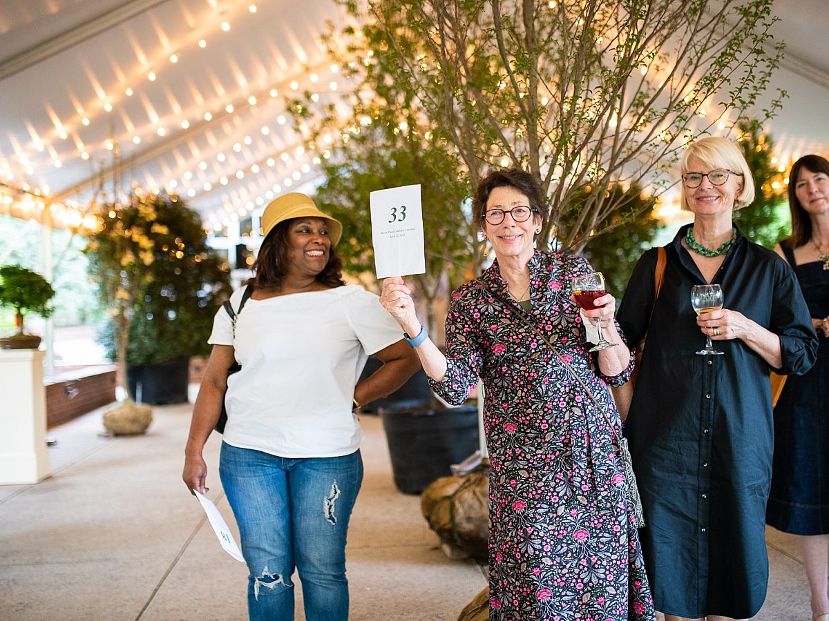 four women outside under a tent with auction sign