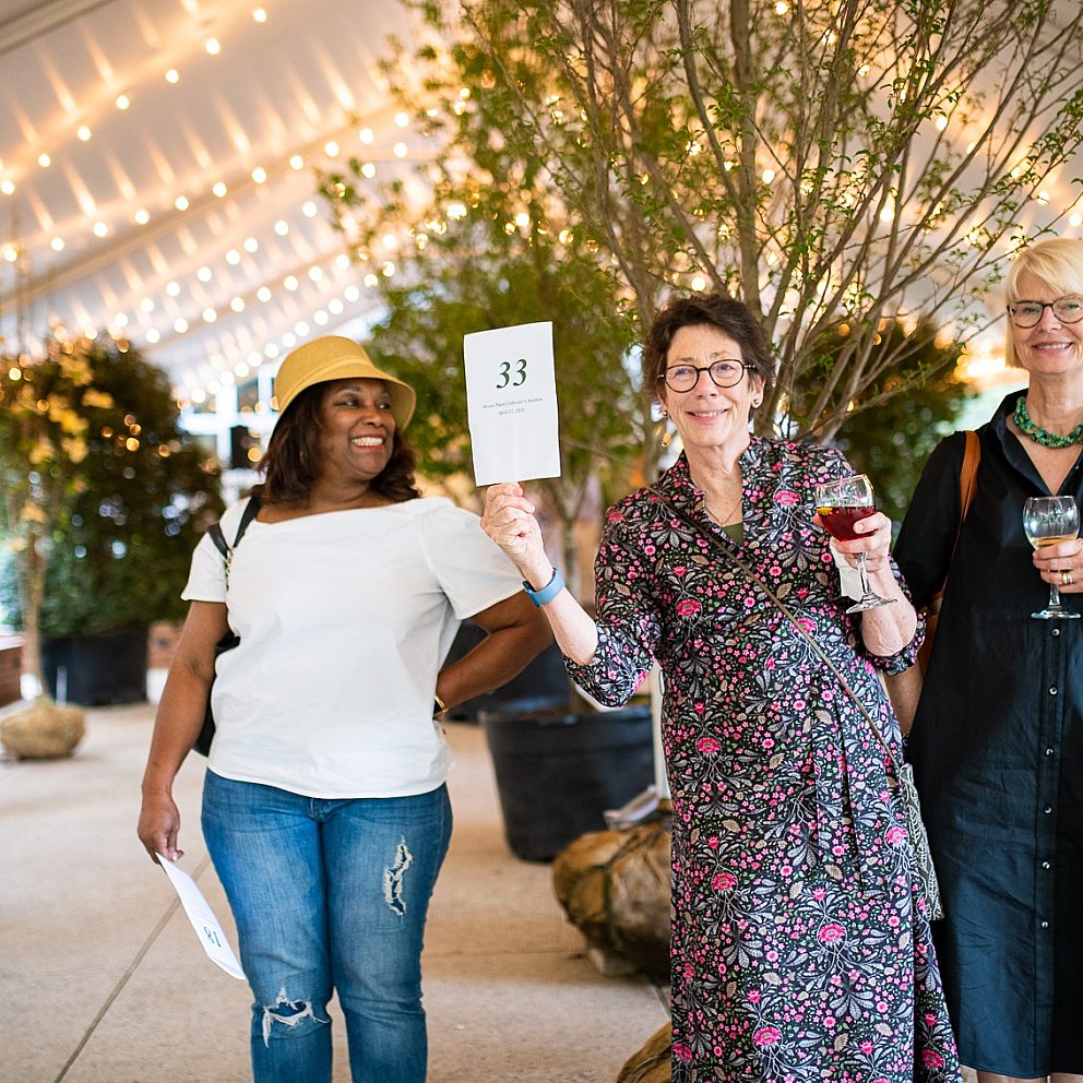 four women outside under a tent with auction sign