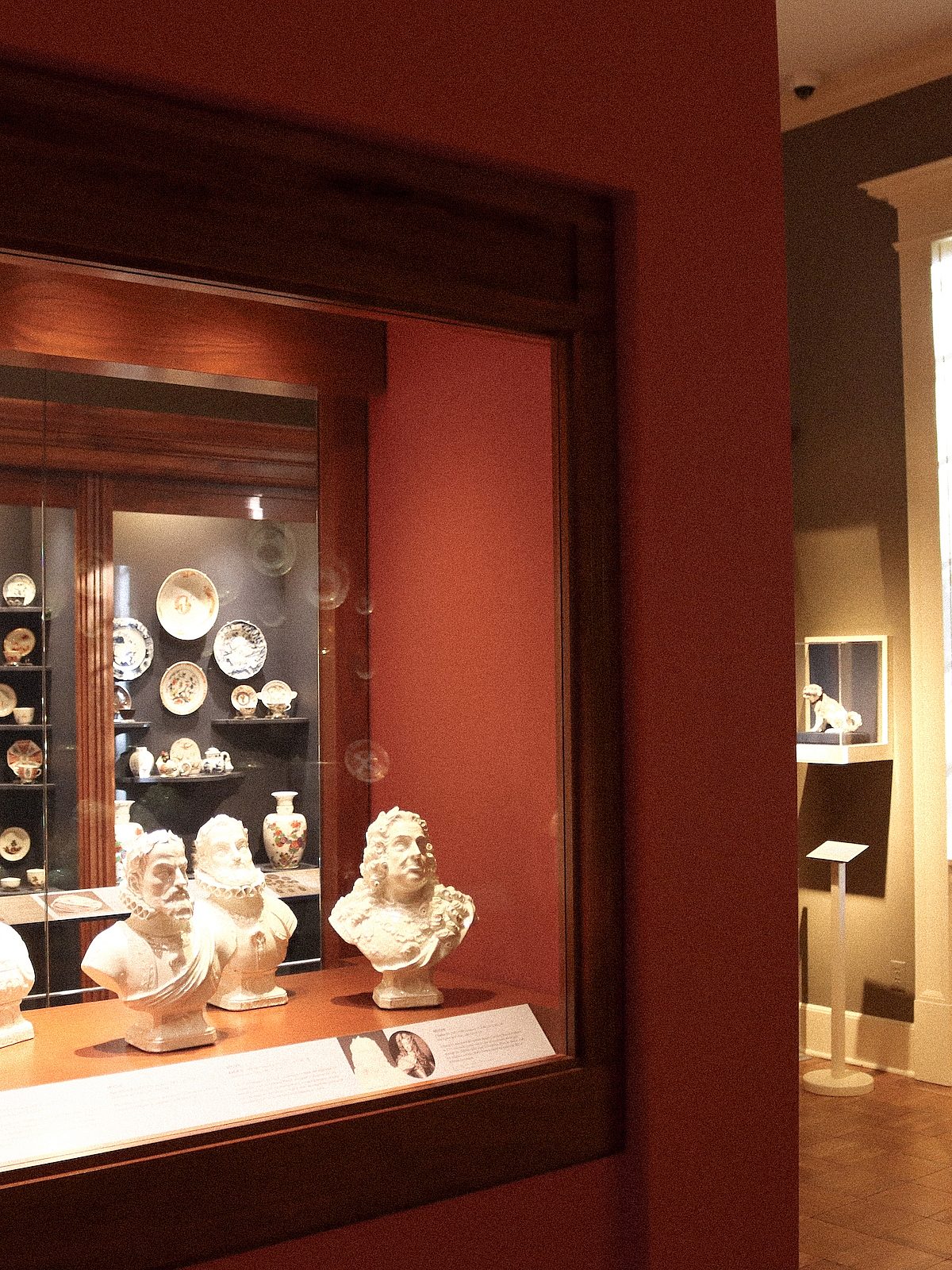 angled red wall with busts and porcelain plates behind display case