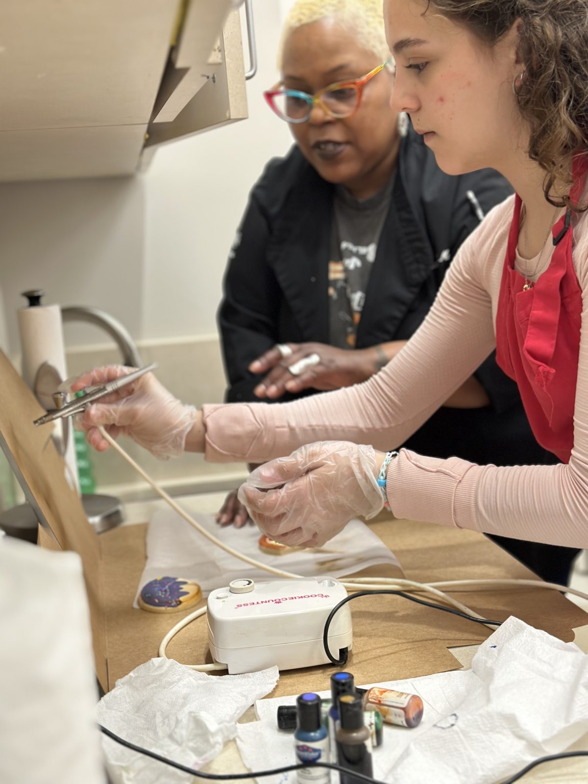 An action photo of a teen working on art, showing the participant, instructor, and artistic medium which is painting