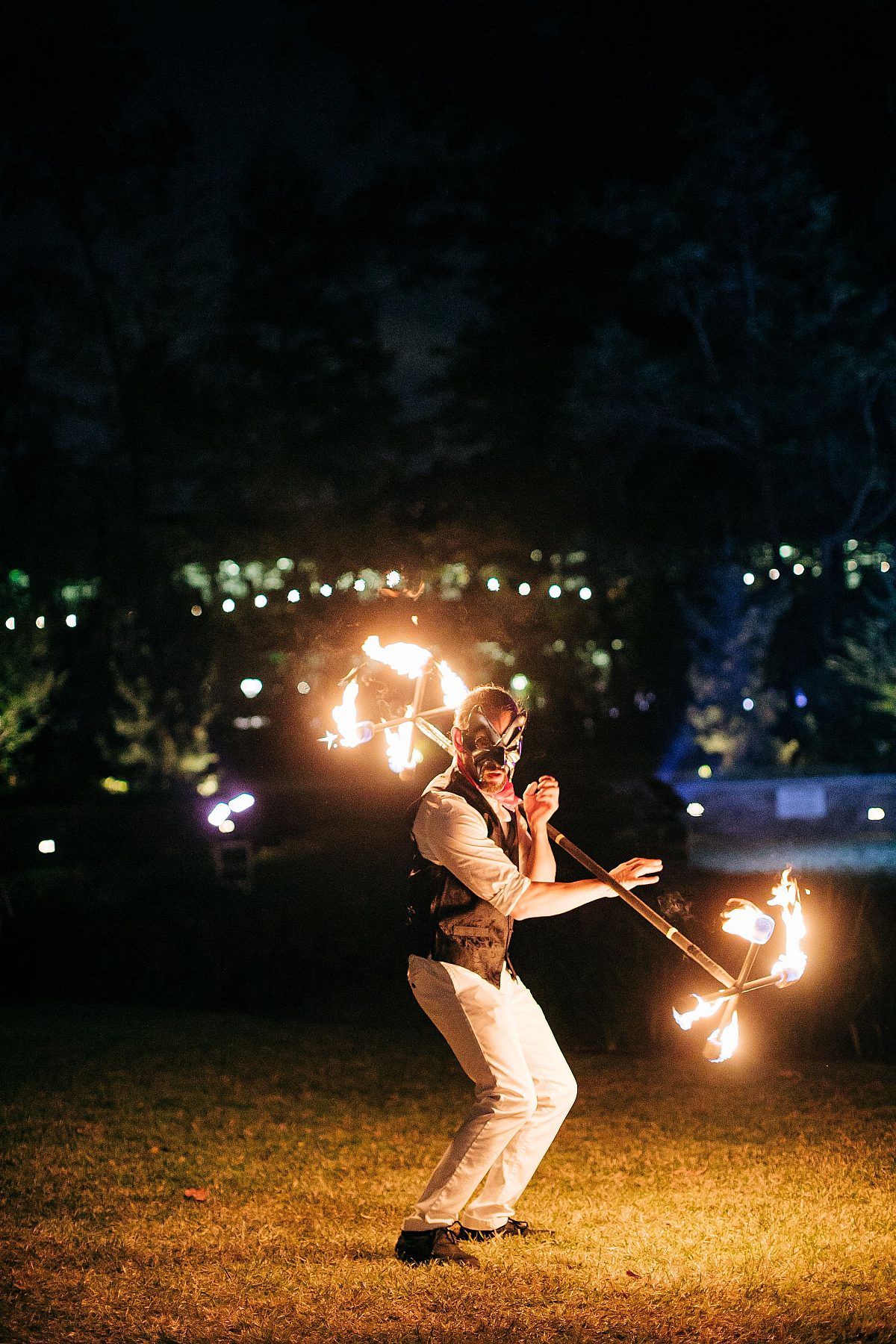 masked man twirling stick with fire. on each end