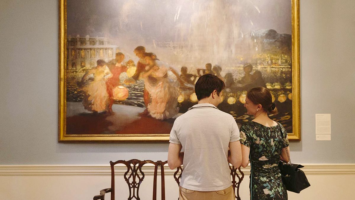couple standing in front of large painting of fireworks on the water