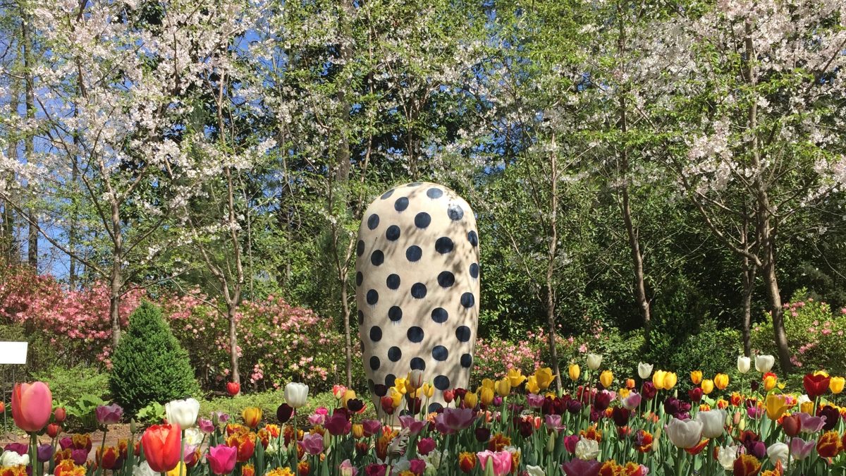 round white sculpture with black dots standing in blooming flower bed of tulips