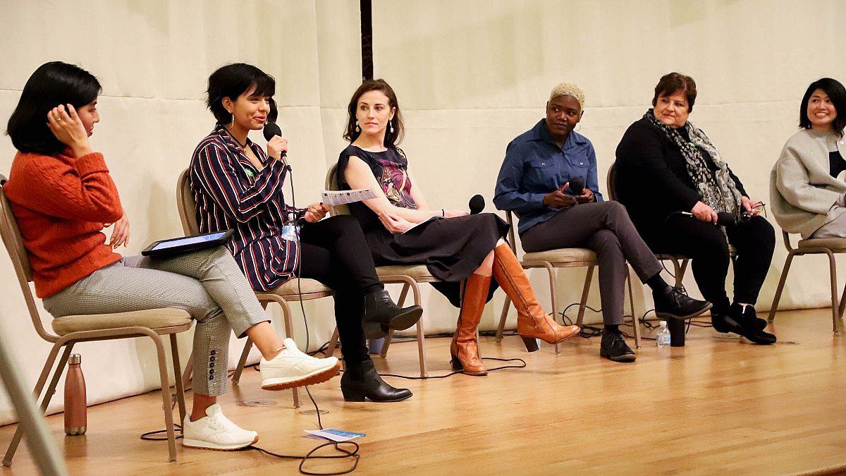 panel of women on stage, one holding a microphone