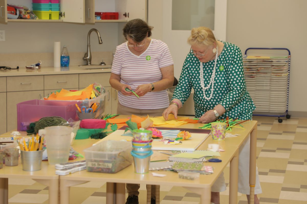 two senior women making tissue paper flowers inside education classroom