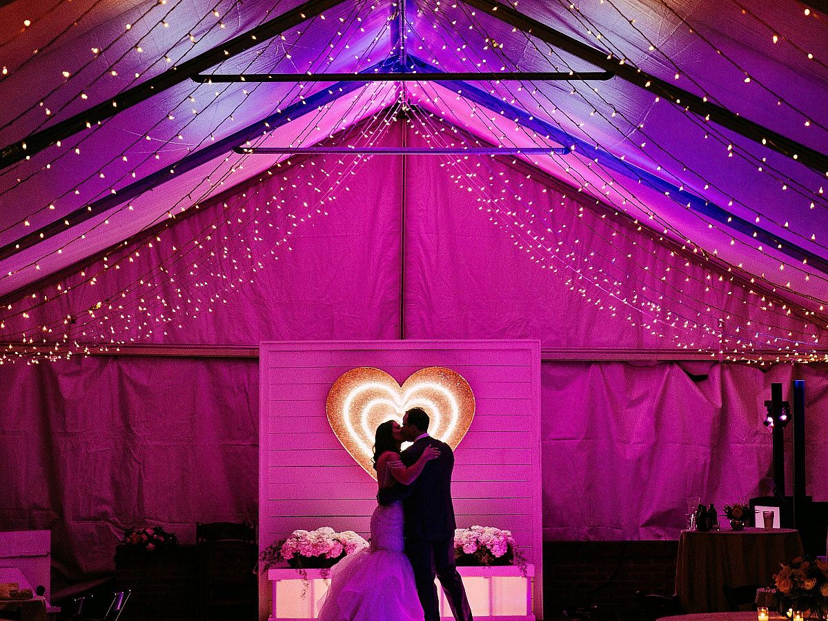 wedding tent lit up pink and purple, couple poses in front of a heart