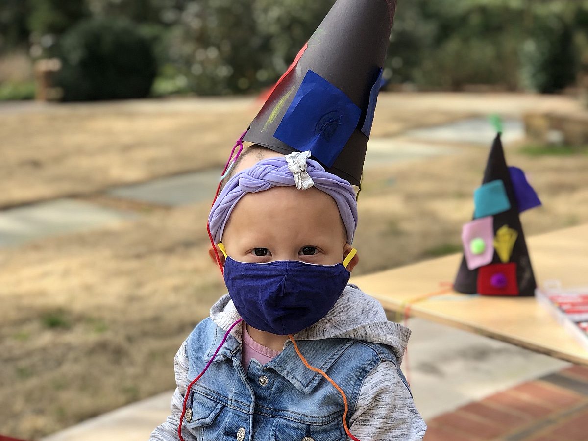 young child wearing mask and hat she crafted