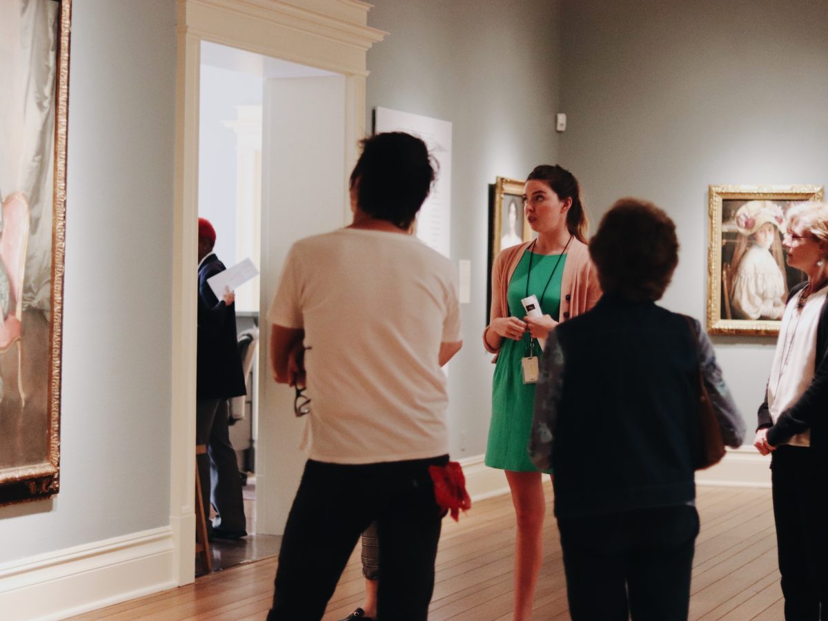 Woman Giving A Tour To Visitors In The Gallery