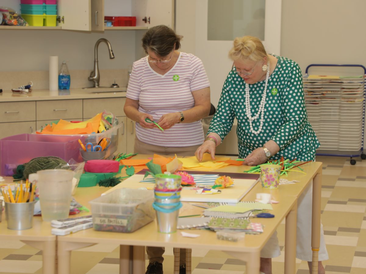 two senior women making tissue paper flowers inside education classroom