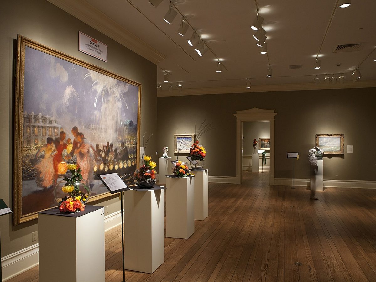 gallery with paintings on wall and flowers presented in front of each