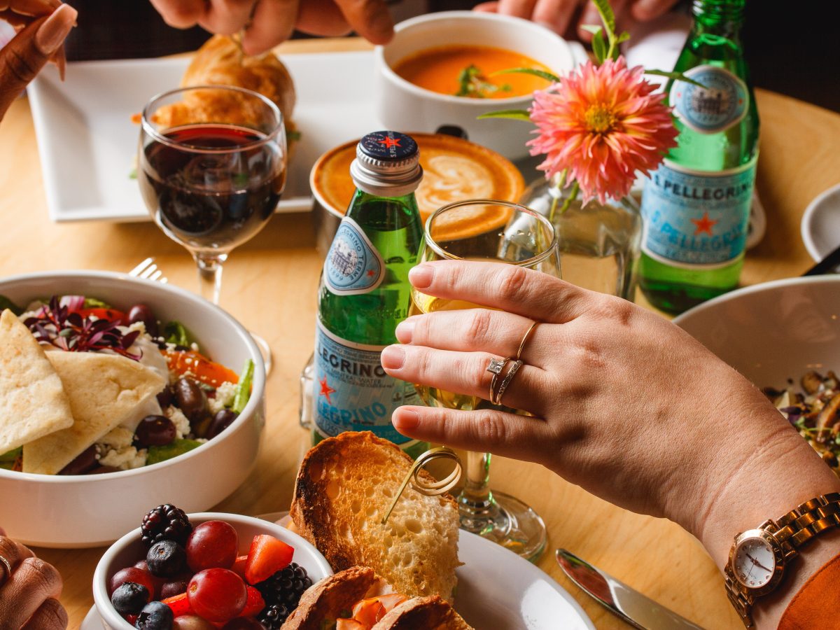 round table laid out for dinner, hands reaching for food and san pellegrino bottles