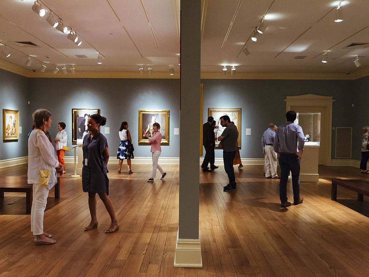 visitors walking around the main gallery with light blue walls and a dividing wall in the middle of the picture