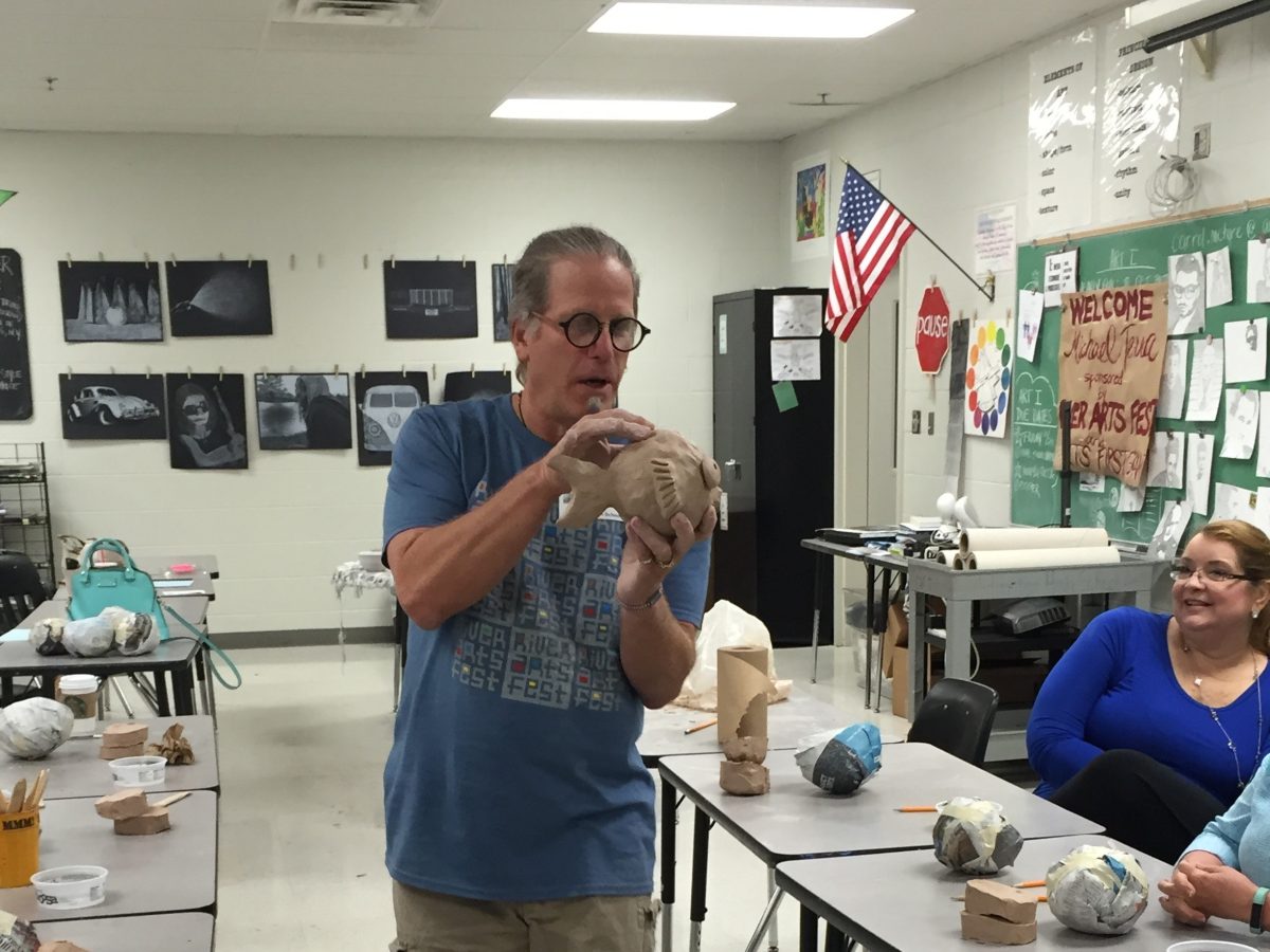 middle-aged man displaying a clay fish to classroom of adults