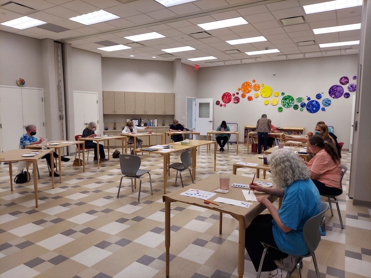 classroom of masked senior citizens, each at individual tables, working on paintings