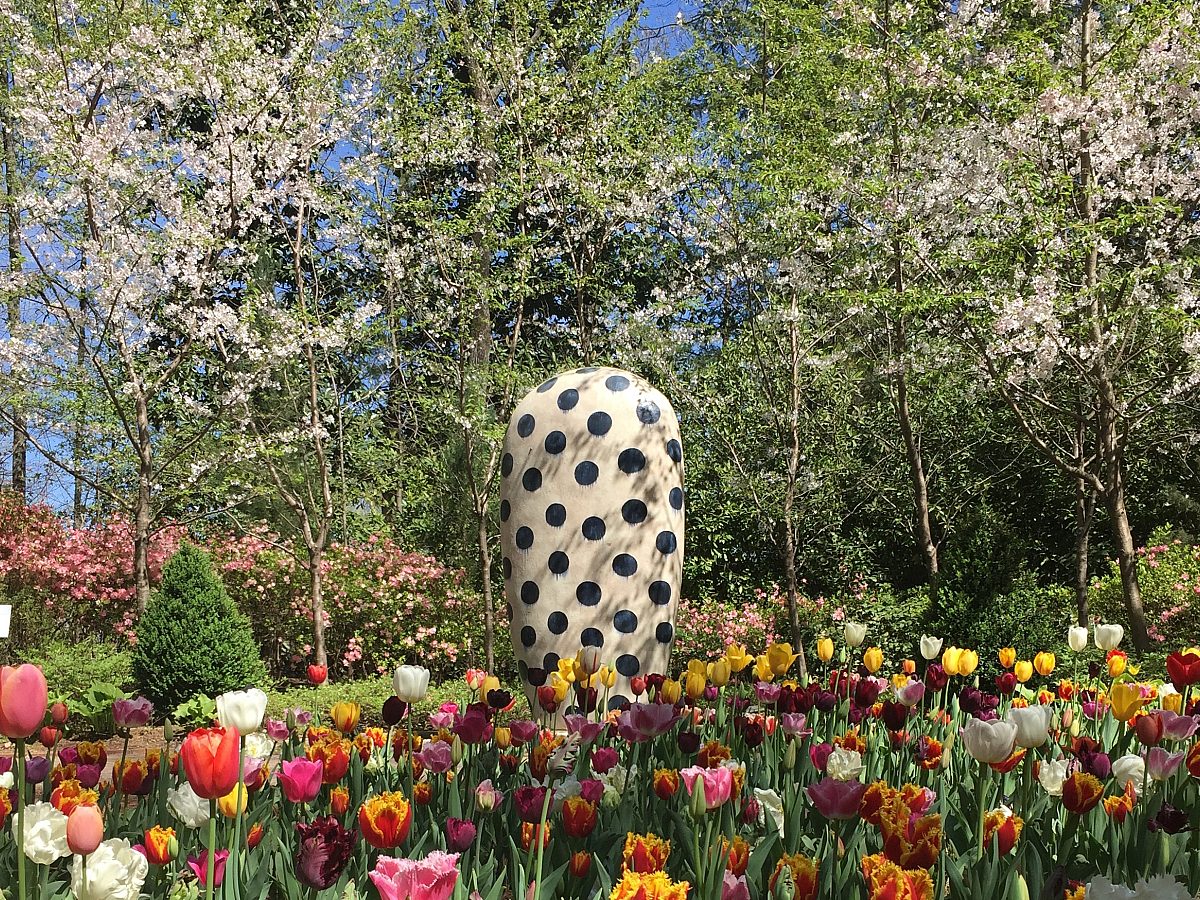 round white sculpture with black dots standing in blooming flower bed of tulips