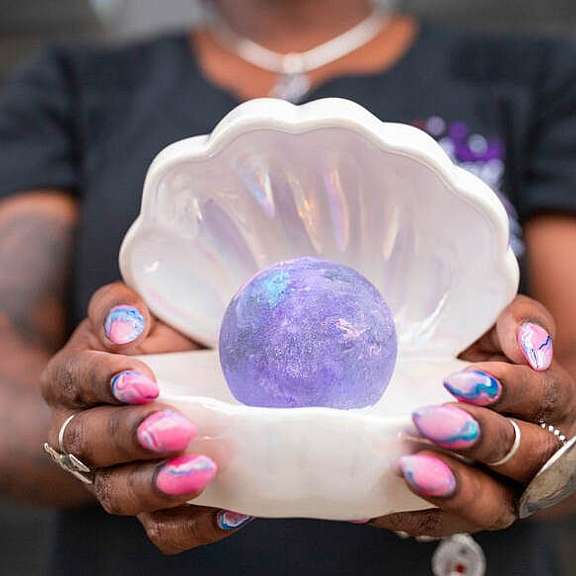 woman with pink and blue designed nails holding a clam shell decoration with purple orb inside