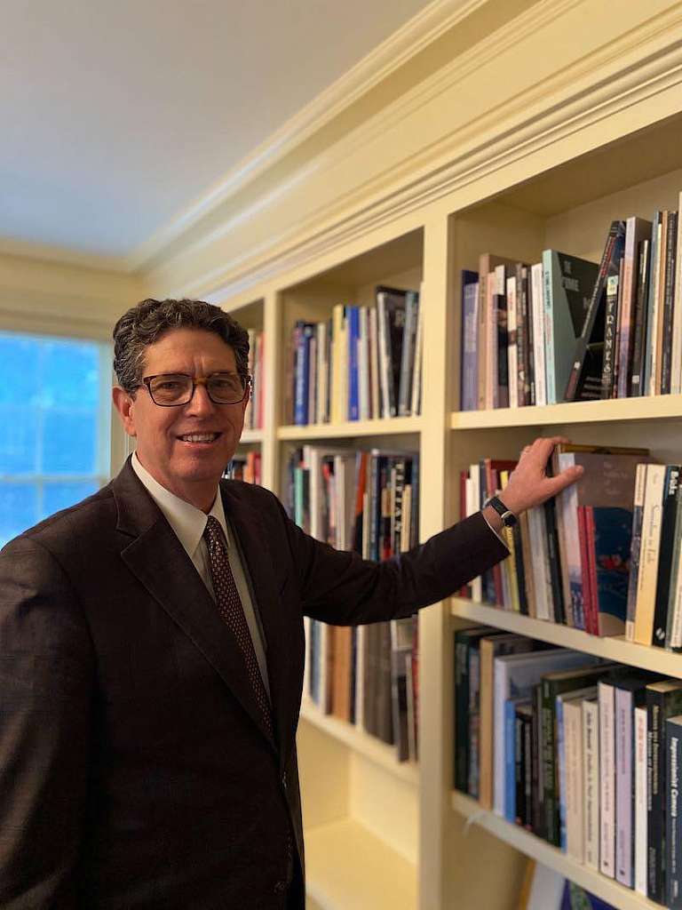 tall man in suit reaching towards large built in bookshelf