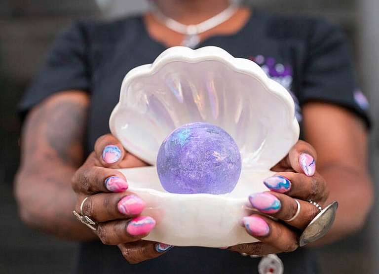 woman with pink and blue designed nails holding a clam shell decoration with purple orb inside